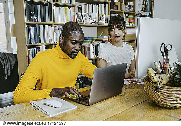 Male freelancer using laptop sitting by woman at table