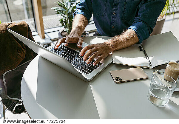 Male freelancer working on laptop at table in cafe