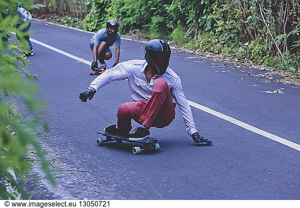Male friends crouching while skateboarding on road