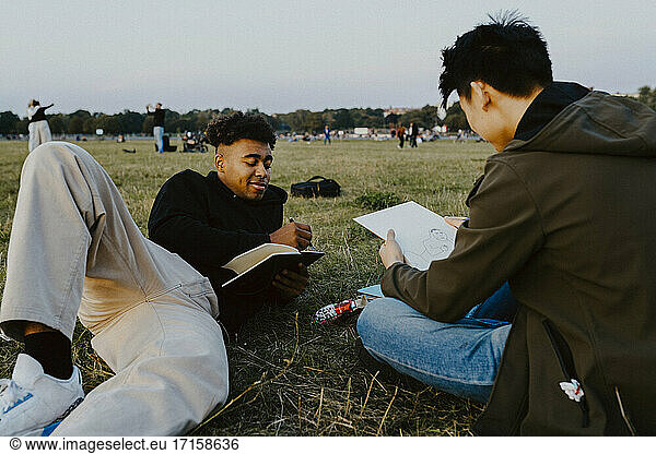 Male friends drawing in book at park during sunset
