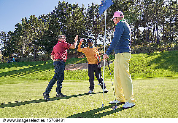 Male friends high fiving on sunny golf course putting green