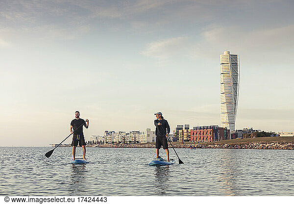 Male friends paddleboarding against sky in sea