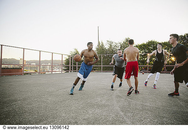 Male friends playing basketball in court against clear sky