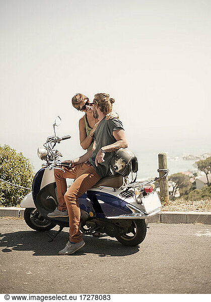 Male friends sitting on motorcycle during sunny day