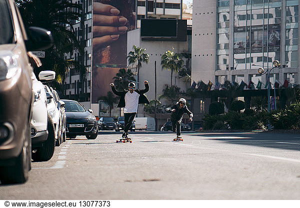 Male friends skateboarding on road in city during sunny day