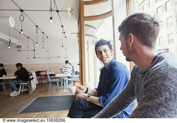 Male friends talking by window at coffee shop