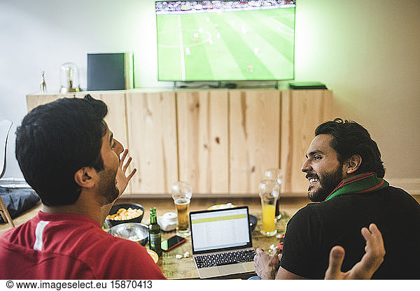 Male friends talking while watching soccer in living room