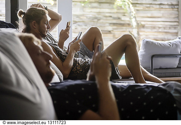 Male friends using mobile phones while relaxing on sofa at home