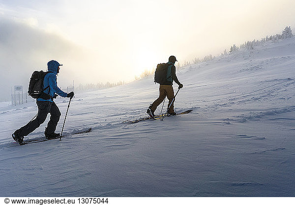 Male friends walking on snow covered field during foggy weather