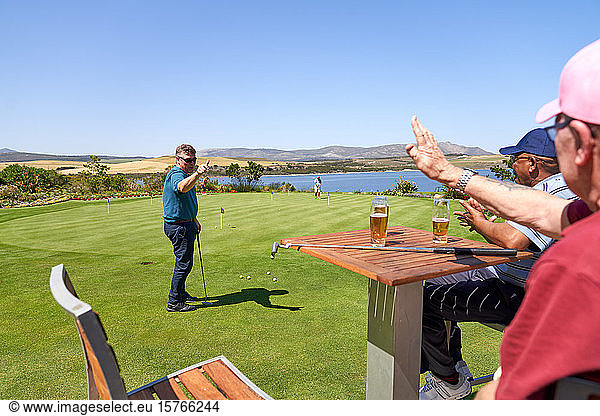 Male golfer friends drinking beer and practicing putting