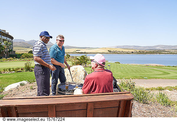 Male golfer friends talking drinking beer on sunny golf course patio