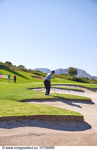 Male golfer preparing to take a shot above sunny golf course bunker