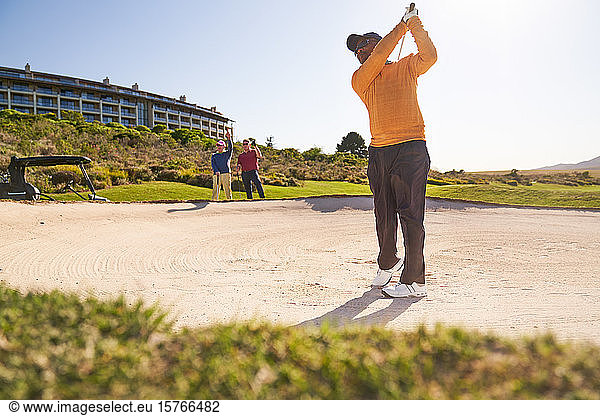 Male golfer taking a shot out of sunny bunker