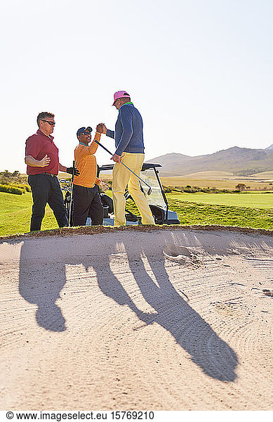 Male golfers celebrating behind sunny golf bunker