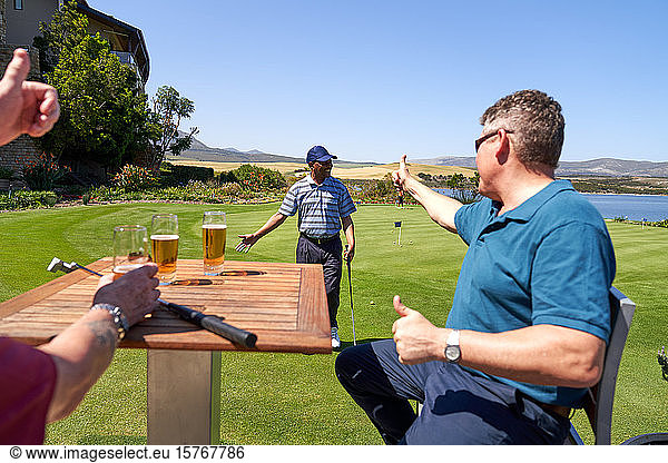 Male golfers drinking beer cheering friend on practice putting green