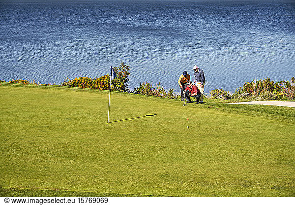 Male golfers planning putt shot at sunny lakeside golf course