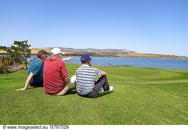 Male golfers relaxing looking at lake view from sunny golf course