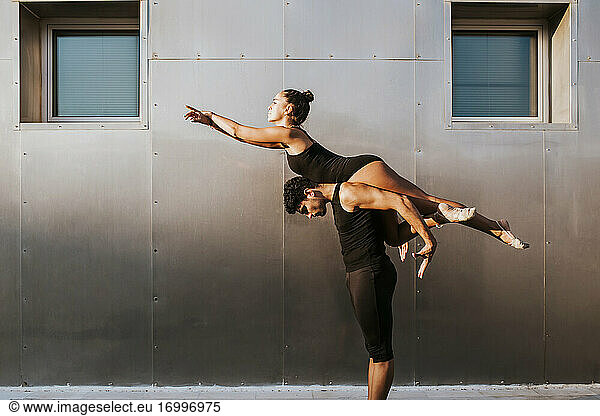 Male gymnast carrying female on shoulders while practicing dance posture by wall