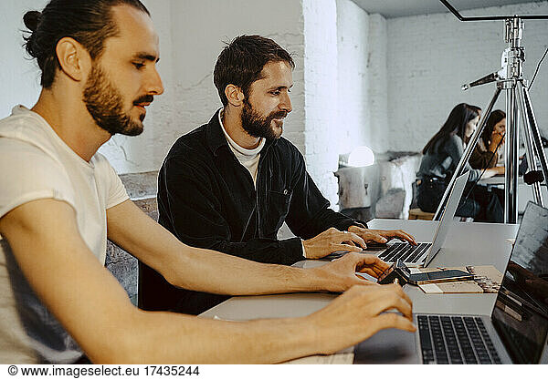 Male hackers working on laptops at desk in creative office