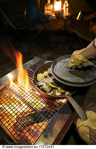 Male hands cooking in a cast-iron over an open fire.