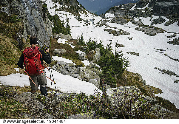 Male hiker descends mountain with poles wearing red backpack  Canada