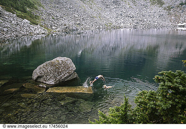 Male hiker diving into alpine lake with dog