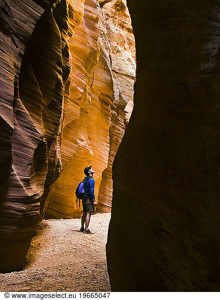Male hiker exploring a narrow sandstone slot canyon.