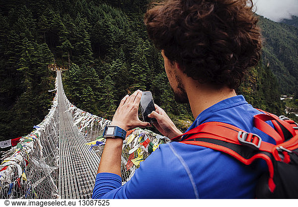 Male hiker photographing footbridge with smart phone at Sagarmatha National Park