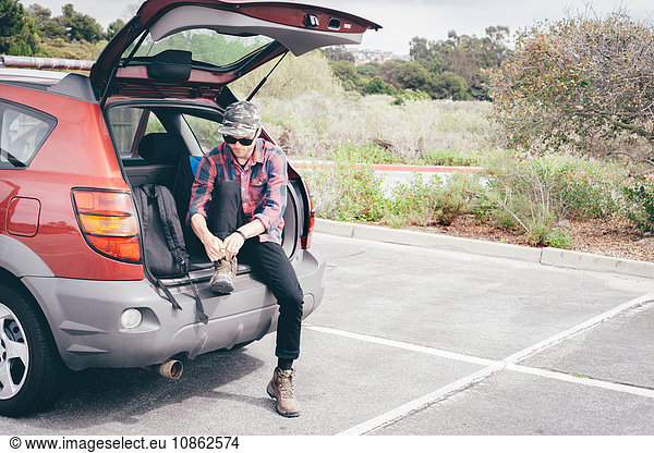 Male hiker sitting on car boot tying hiking boot laces  Crystal Cove State Park  Laguna Beach  California  USA