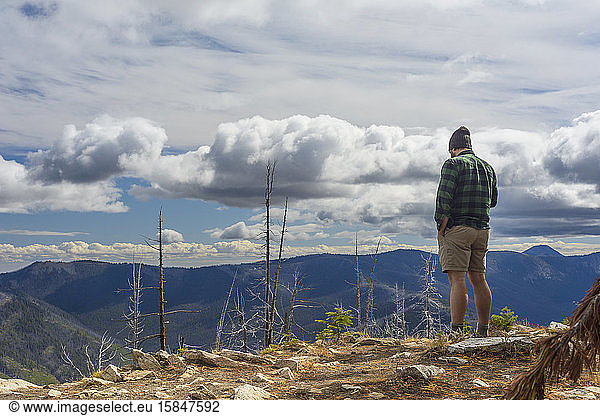 Male Hiker Standing On Mountain Top With Dramatic Clouds