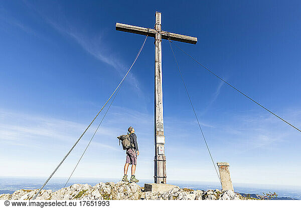 Male hiker standing under summit cross on Benediktenwand
