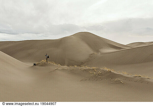 male hiker walks in sand dunes and grasses on a cloudy day in colorado