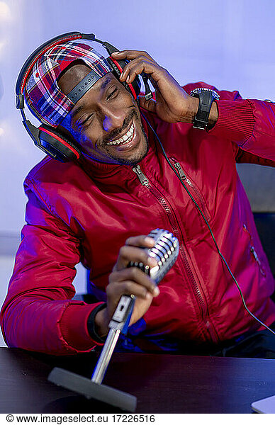 Male influencer wearing headphones and holding microphone during podcast in studio