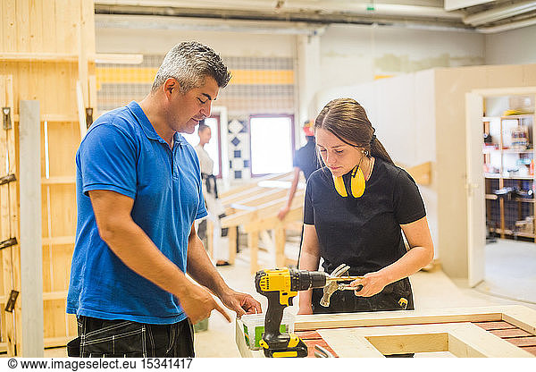 Male instructor teaching female trainee at workbench in illuminated workshop