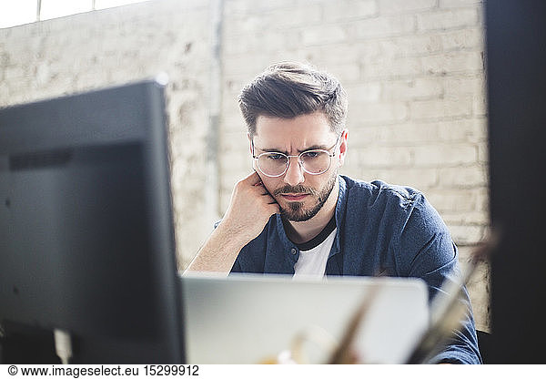 Male IT professional thinking while working on computer codes in laptop at workplace
