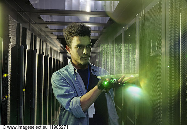 Male IT technician holding glowing futuristic digital tablet in server room