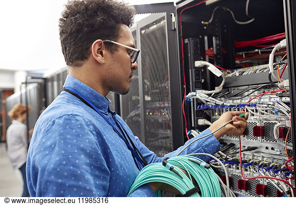 Male IT technician plugging cable into panel in server room