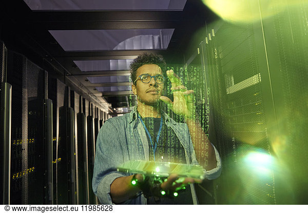 Male IT technician using futuristic digital tablet in dark server room