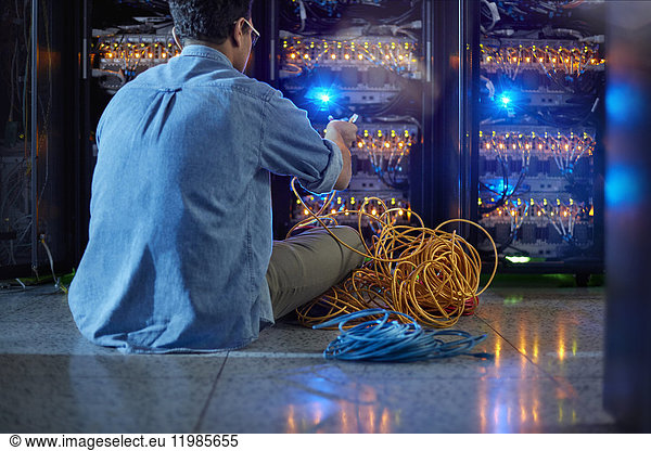 Male IT technician with cables at panel in dark server room