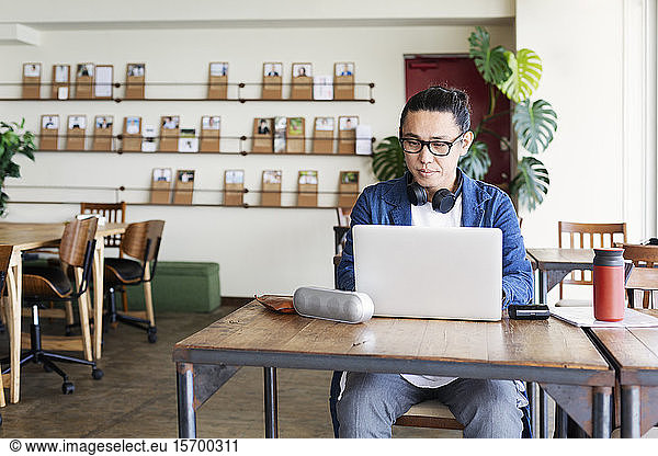 Male Japanese professional sitting at a table in a co-working space  using laptop computer.