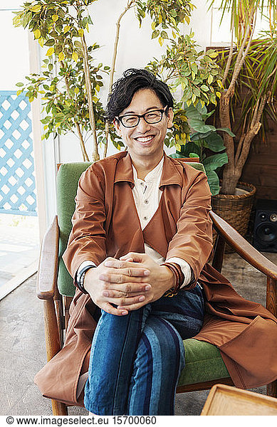 Male Japanese professional sitting in a co-working space  smiling at camera.