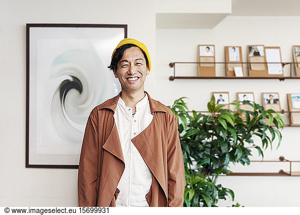 Male Japanese professional standing in a co-working space  smiling at camera.