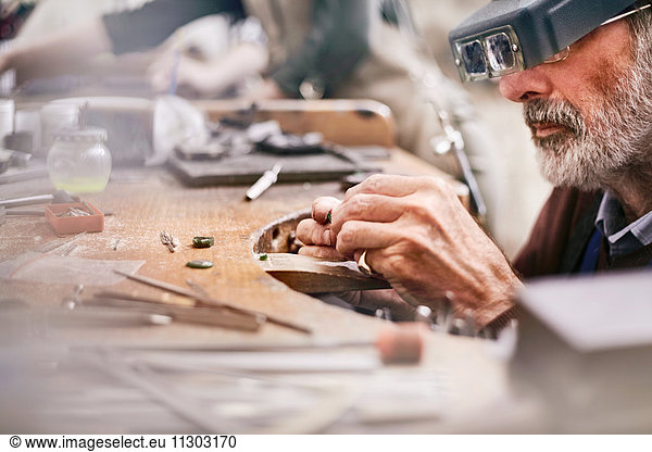 Male jeweler using headband magnifier making jewelry in workshop