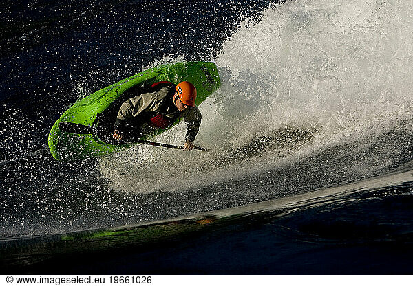 Male kayaker playboating on a large wave in nice light.