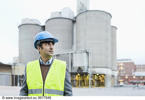 Male manual worker looking away while standing against cement silos