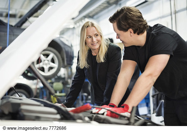 Male mechanic discussing with female customer while repairing car engine at workshop