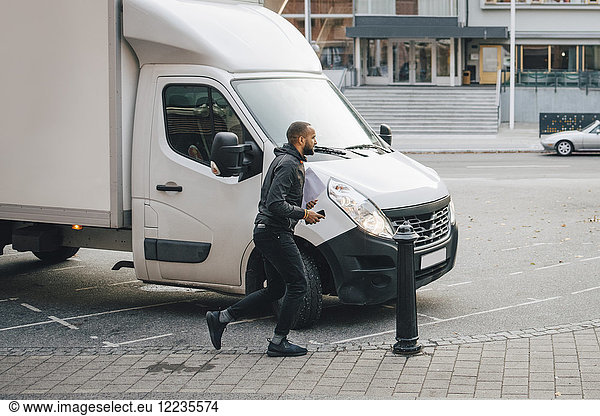 Male messenger with documents running by delivery van on street in city