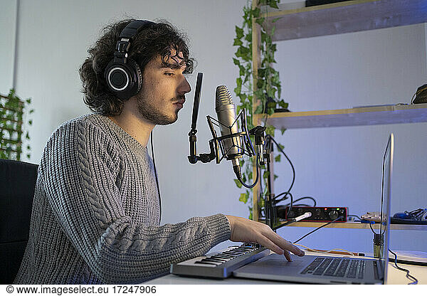 Male music composer with sound recording equipment using laptop at home