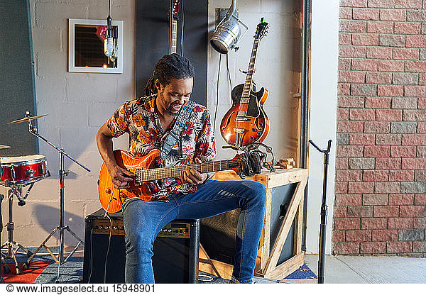 Male musician playing electric guitar in garage recording studio