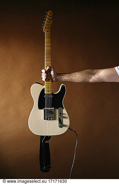 Male musician's hand holding guitar against wall